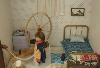 Doll in old-fashioned bedroom spinning on great wheel.